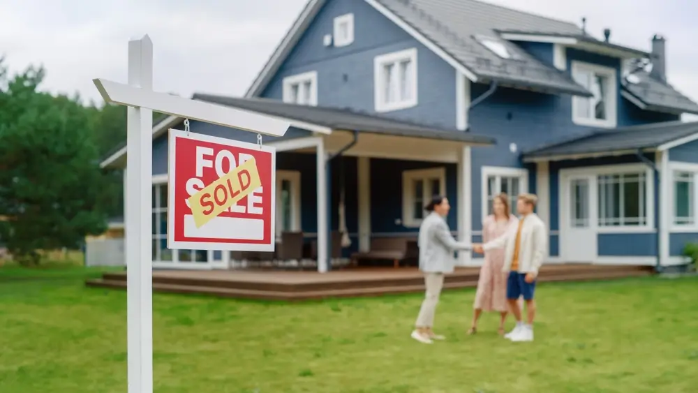 real estate agent and buyers in front of sold home sign and house