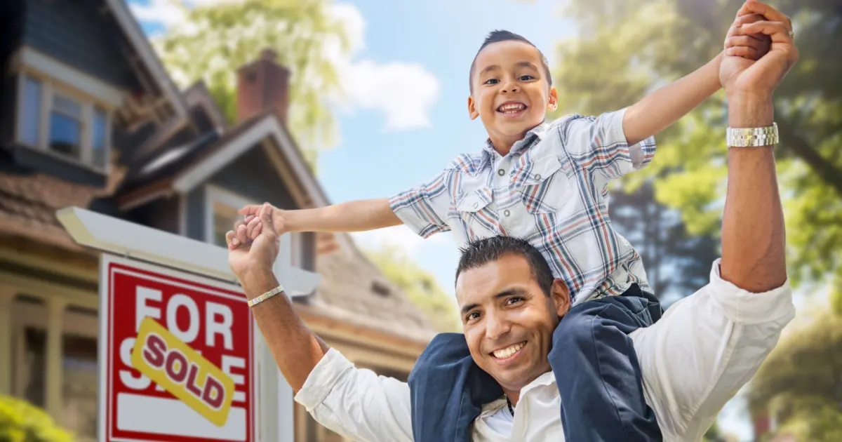 Father and son celebrating in front of home with sold sign